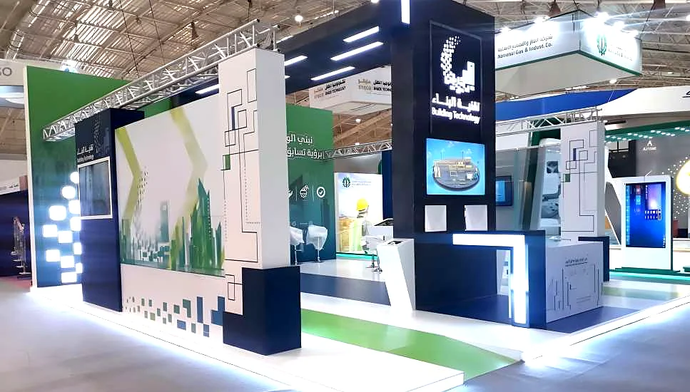 Modern Construction exhibition booth with illuminated white counters, green branding and navy towers
